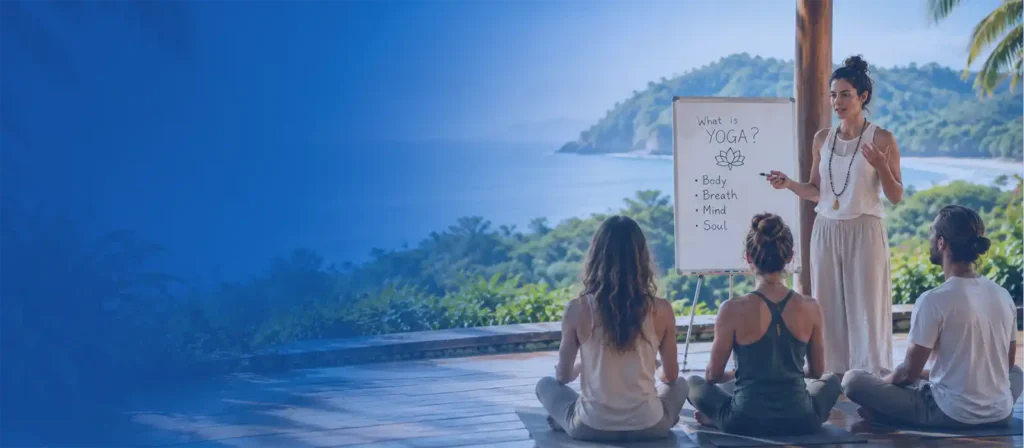 How to Choose Yoga Teacher Training - Yoga teacher explaining concepts to TTC students during an outdoor yoga teacher training class in a tropical Goa-style learning environment.